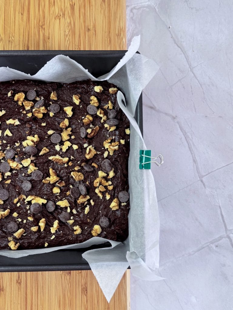 Compoziție de brownie cu cartof dulce, cu dropsuri de ciocolată și nuci deasupra, într-o tavă tapetată cu hârtie de copt, înainte de a fi pusă la cuptor