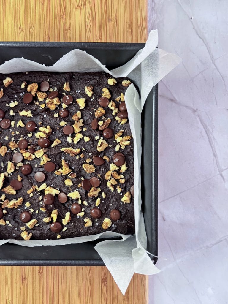Brownie cu cartof dulce copt, cu dropsuri de ciocolată, nuci și fulgi de sare deasupra, în tava tapetată cu hârtie de copt