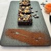 Sliced sweet potato brownie topped with walnuts, chocolate and sea salt, arranged on a slate platter dusted with cocoa, next to mashed sweet potato and coffee