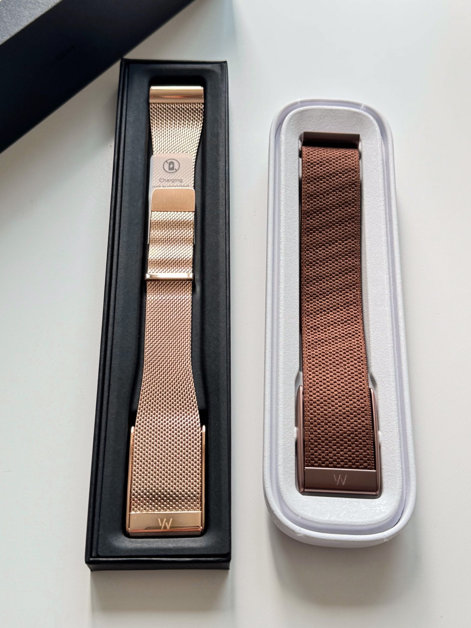 Două brățări Whoop, una din metal rose gold și una textil maro, prezentate în cutiile lor