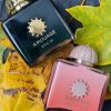 Parfumurile Amouage Epic 56, în sticlă verde închis, și Guidance 46, în sticlă roz, așezate pe frunze galbene de toamnă