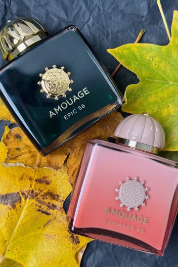 Parfumurile Amouage Epic 56, în sticlă verde închis, și Guidance 46, în sticlă roz, așezate pe frunze galbene de toamnă
