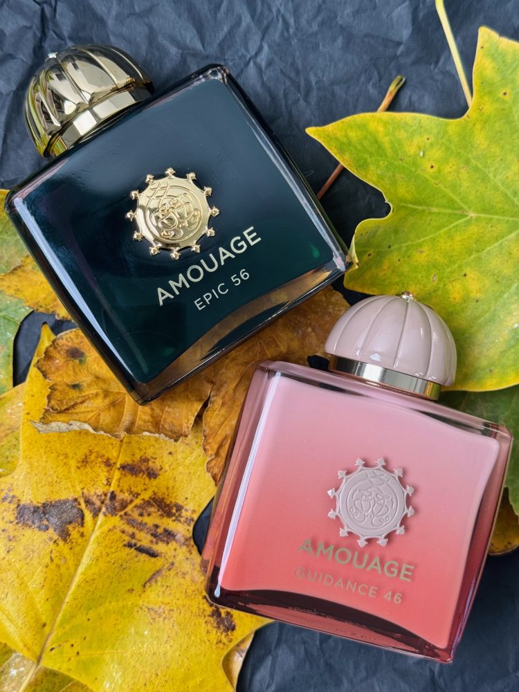Parfumurile Amouage Epic 56, în sticlă verde închis, și Guidance 46, în sticlă roz, așezate pe frunze galbene de toamnă