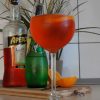 Glass of Aperol Spritz with Aperol and sparkling water bottles behind it and orange pieces on a wooden board
