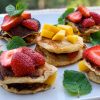 Clătite cu banane și ouă, fără făină, servite cu bucăți de mango, căpșuni proaspete și frunze de mentă