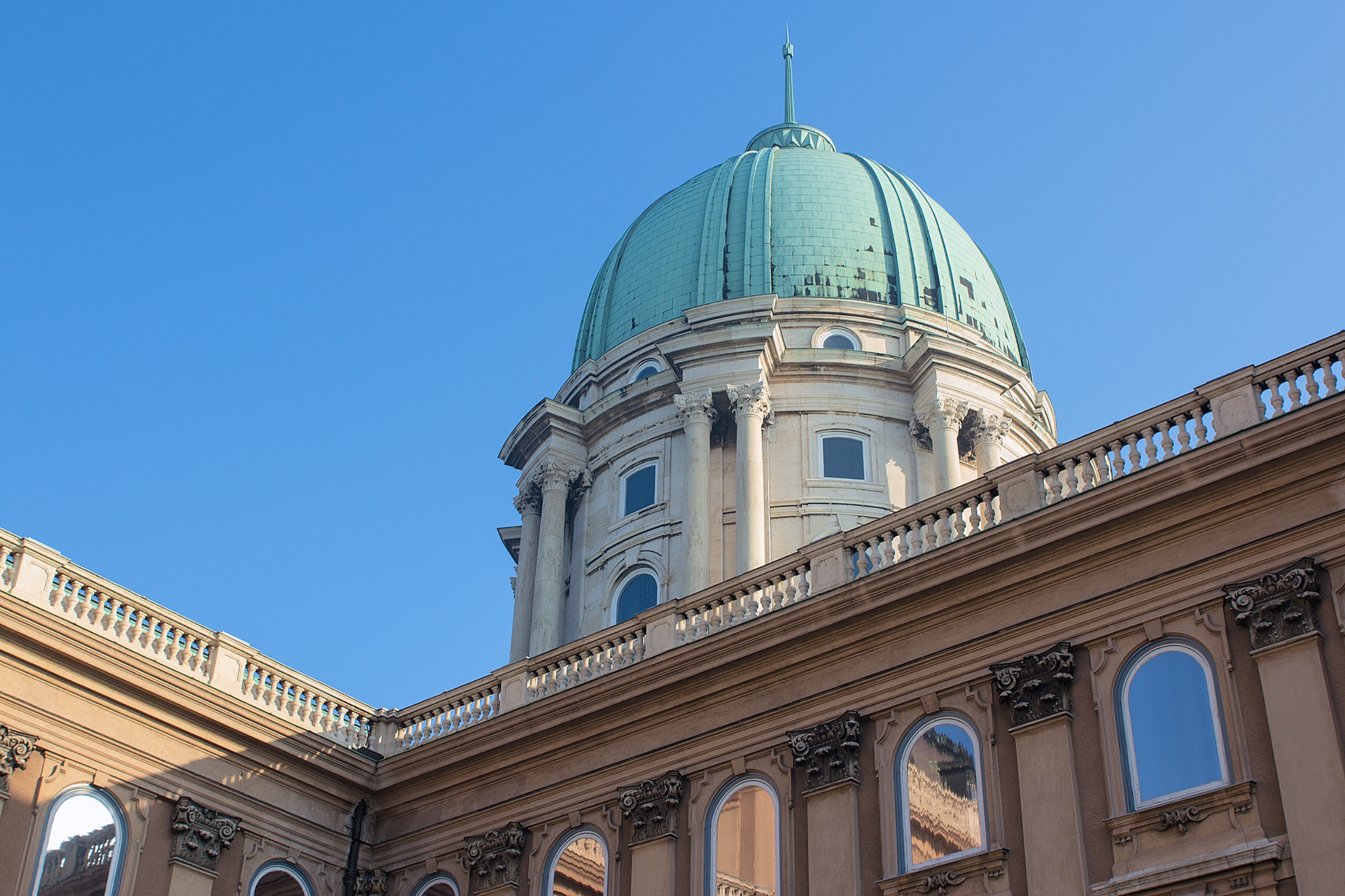 The green dome of Buda Castle rising above its pale façade against a blue sky
