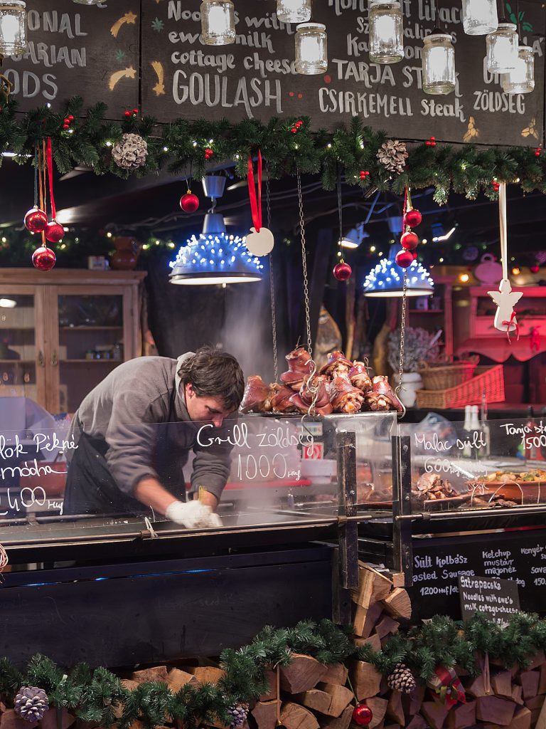 A cook working at a garland-decorated food stall with firewood stacked underneath