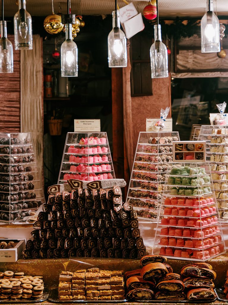 Pastries and stacked boxes of sweets displayed beneath hanging lamps at a market stall