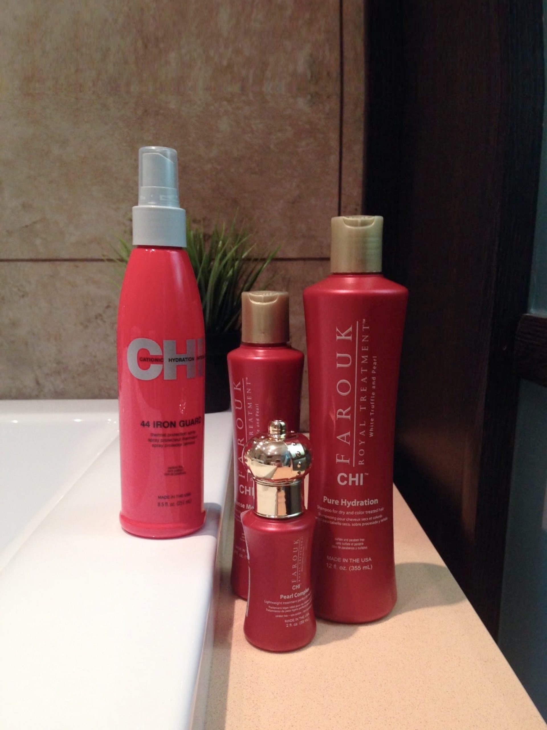 CHI Royal Treatment shampoo, hair mask and Pearl Complex hair oil, alongside 44 Iron Guard spray, arranged beside a bathtub
