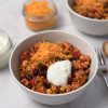 Close-up of chicken chilli con carne with red kidney beans and sweetcorn, topped with shredded cheddar cheese and sour cream