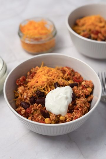 Close-up of chicken chilli con carne with red kidney beans and sweetcorn, topped with shredded cheddar cheese and sour cream