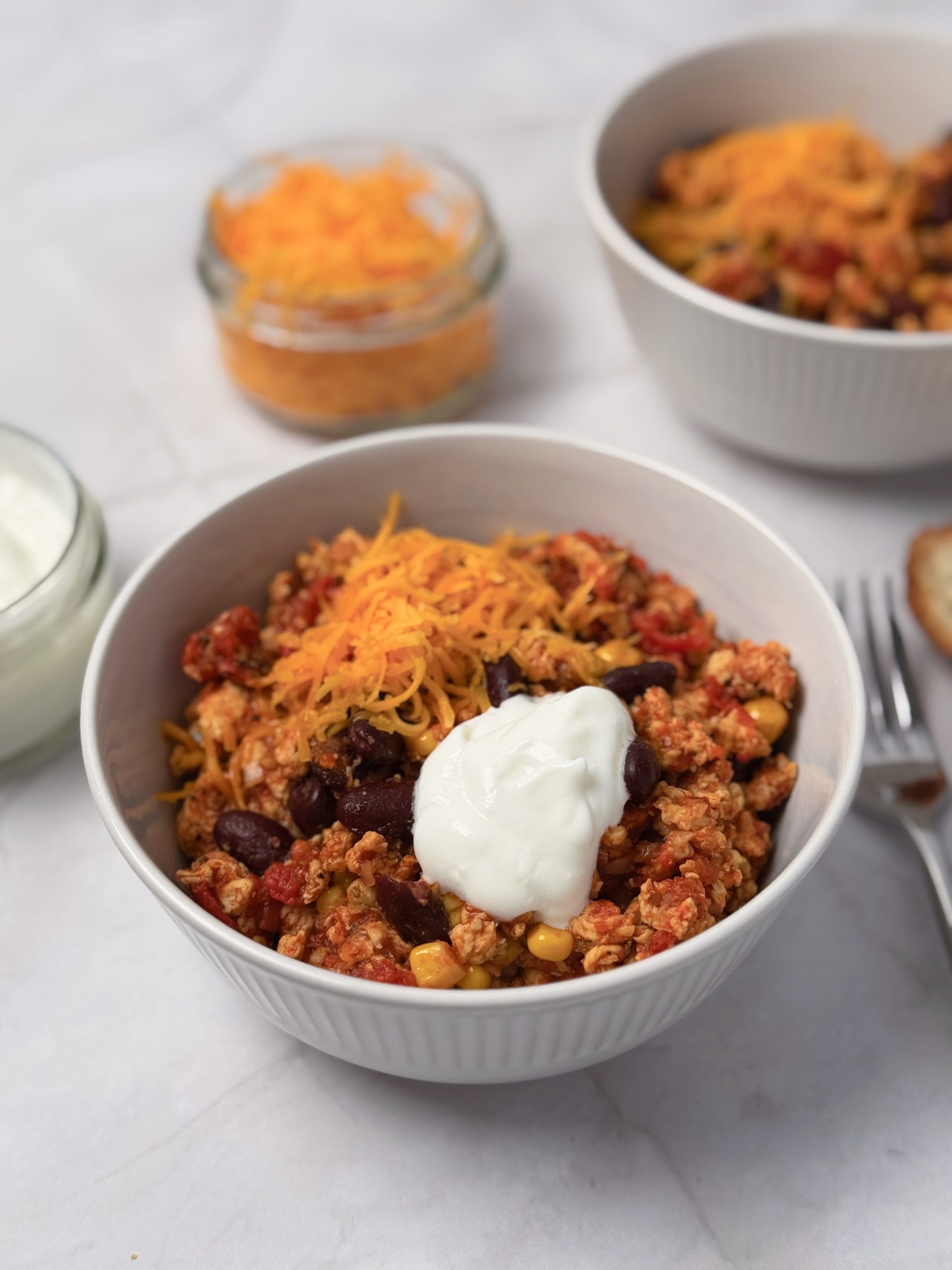 Close-up of chicken chilli con carne with red kidney beans and sweetcorn, topped with shredded cheddar cheese and sour cream