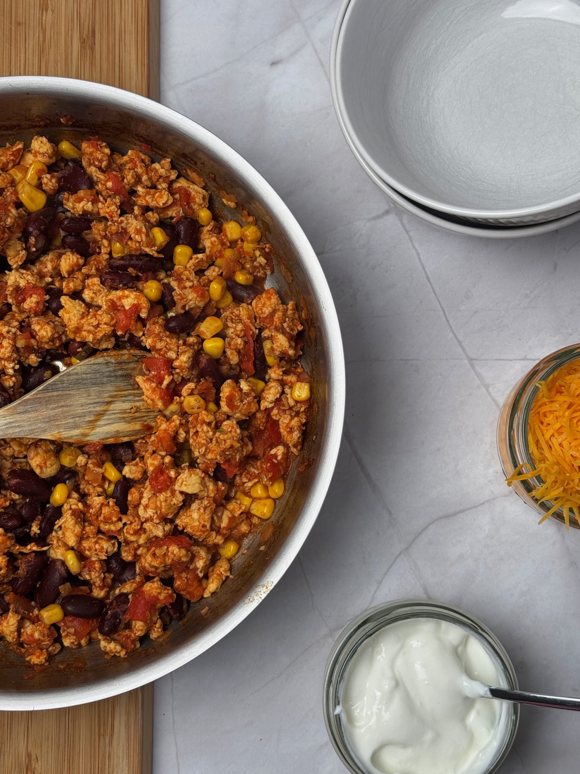 Chicken chilli con carne with kidney beans and sweetcorn in a pan, served with sour cream and grated cheddar cheese