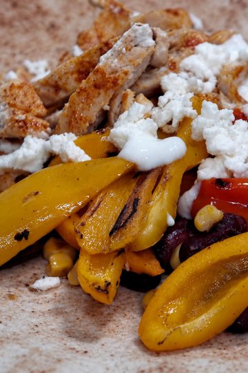 Chicken and vegetable tortilla topped with feta and yogurt, with yellow and red peppers, kidney beans and sweetcorn