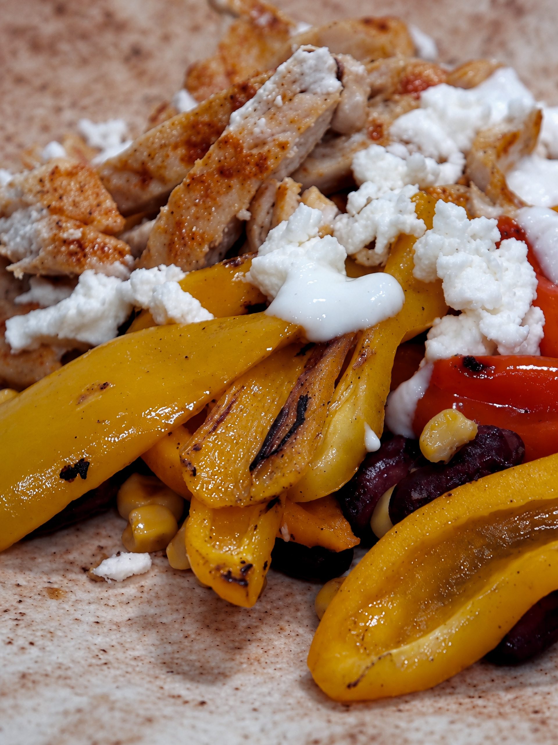 Chicken and vegetable tortilla topped with feta and yogurt, with yellow and red peppers, kidney beans and sweetcorn