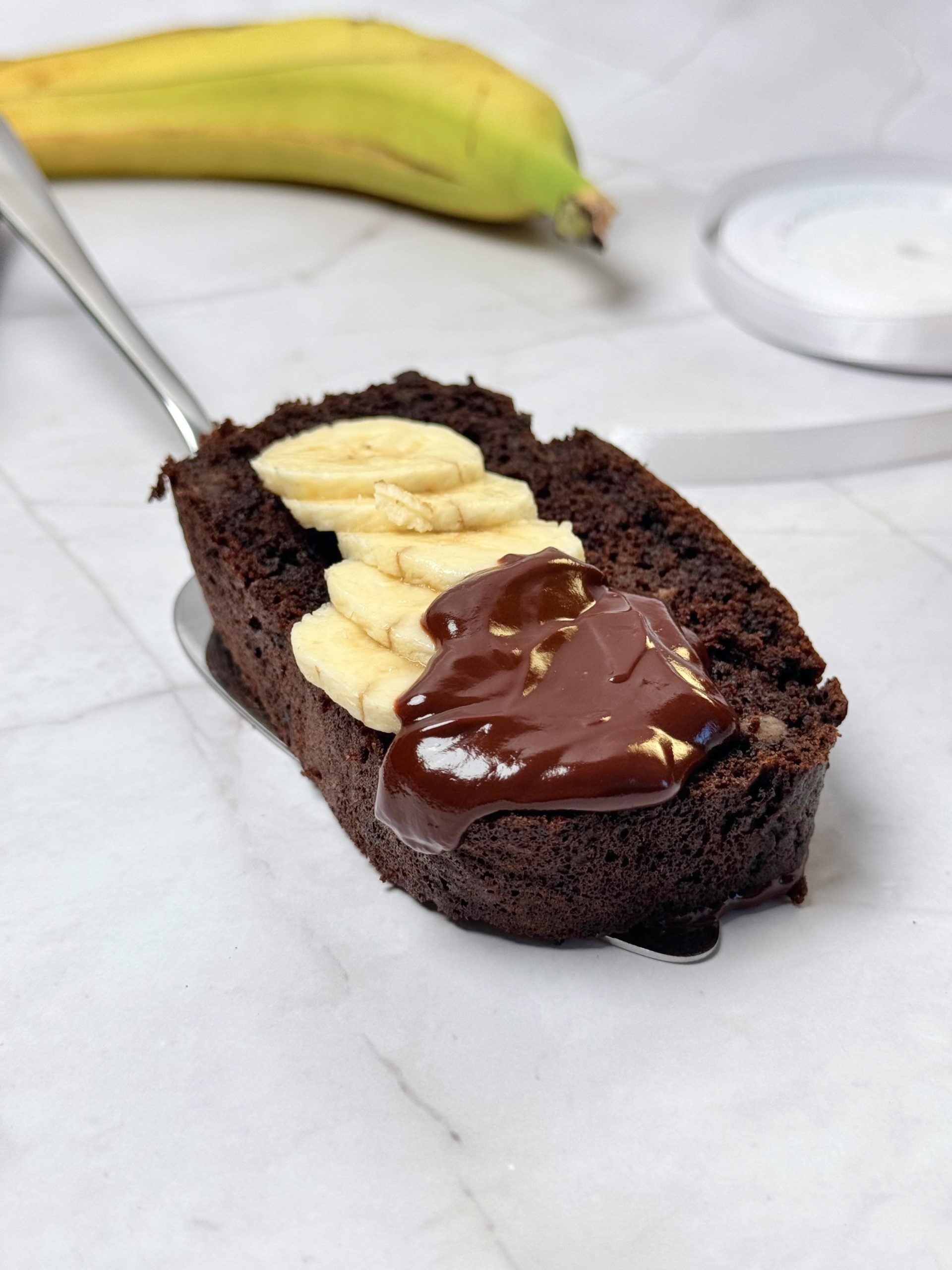 Felie de chec cu banane și ciocolată, decorată cu felii proaspete de banană și ganache cremos de ciocolată