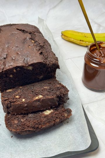 Chec cu banane și ciocolată, tăiat în felii, alături de un borcan cu ganache cremos de ciocolată și o banană