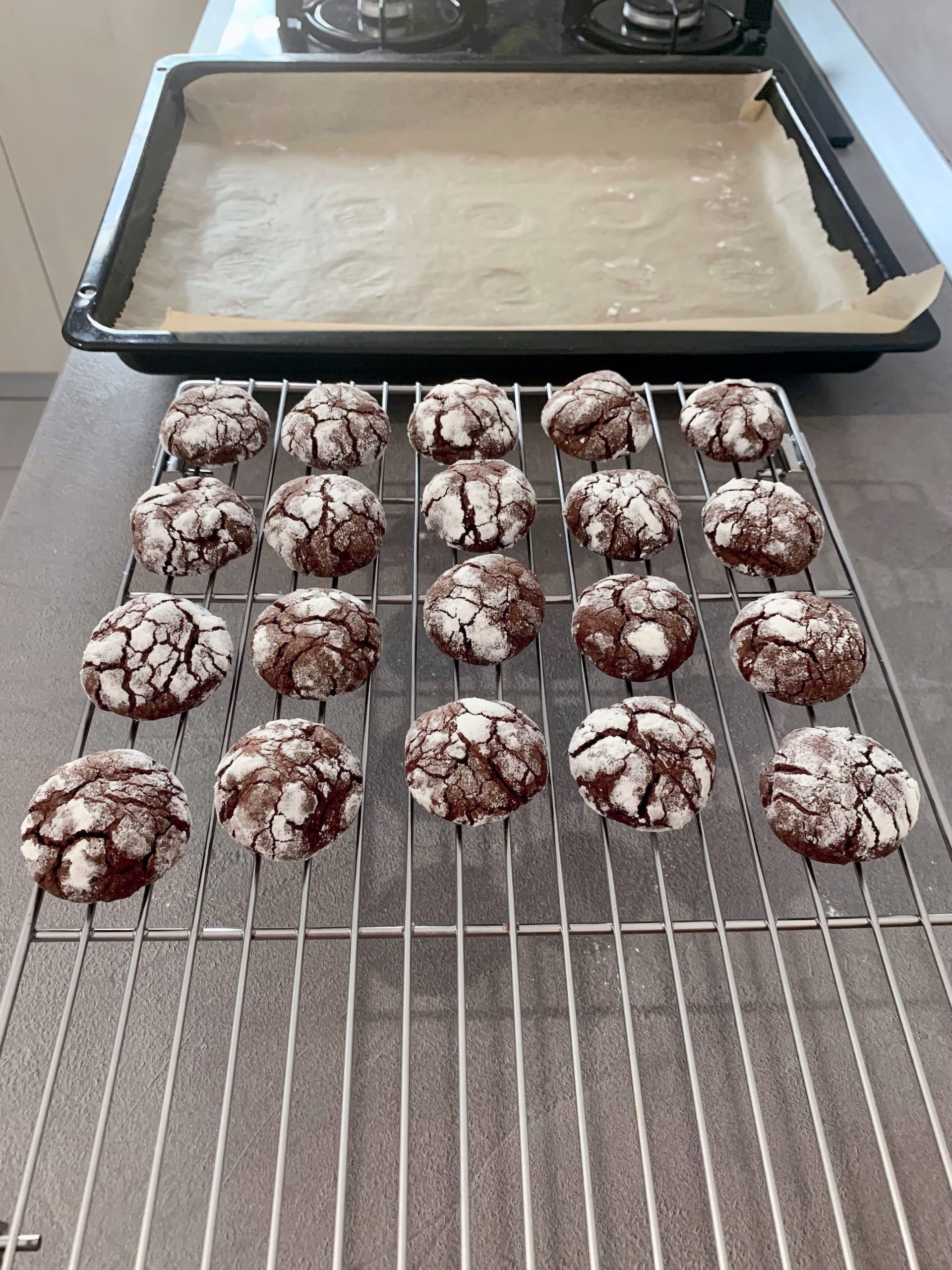 Freshly baked chocolate crinkle cookies coated in powdered sugar, cooling on a wire rack