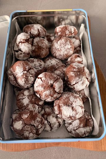 Homemade chocolate crinkle cookies coated in powdered sugar and arranged in a metal tin