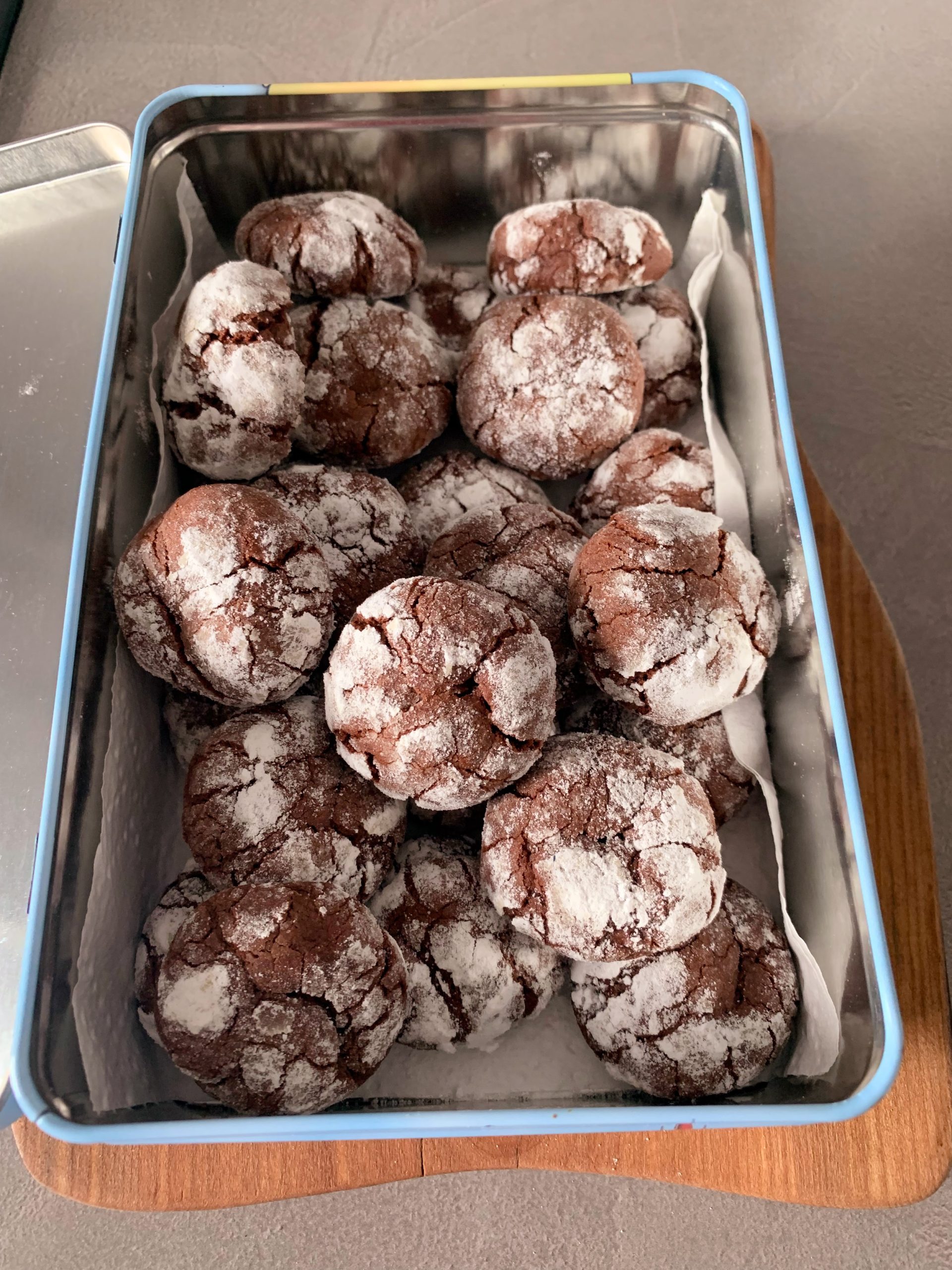 Homemade chocolate crinkle cookies coated in powdered sugar and arranged in a metal tin