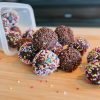 Cocoa balls coated with brown and colorful sprinkles on a wooden board