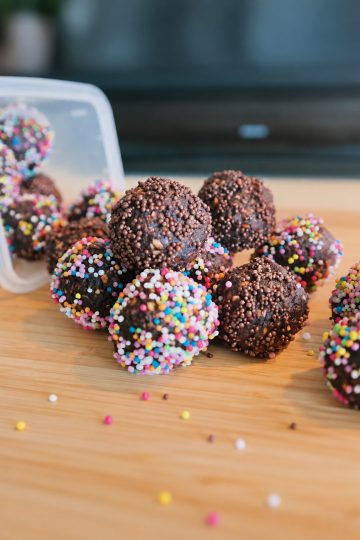 Cocoa balls coated with brown and colorful sprinkles on a wooden board