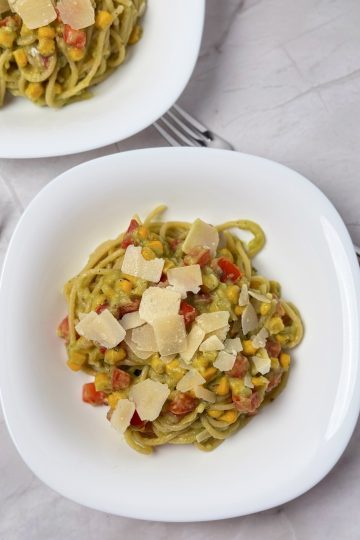 Creamy avocado spaghetti with sweet corn, diced tomatoes and shaved Parmesan, served in white bowls