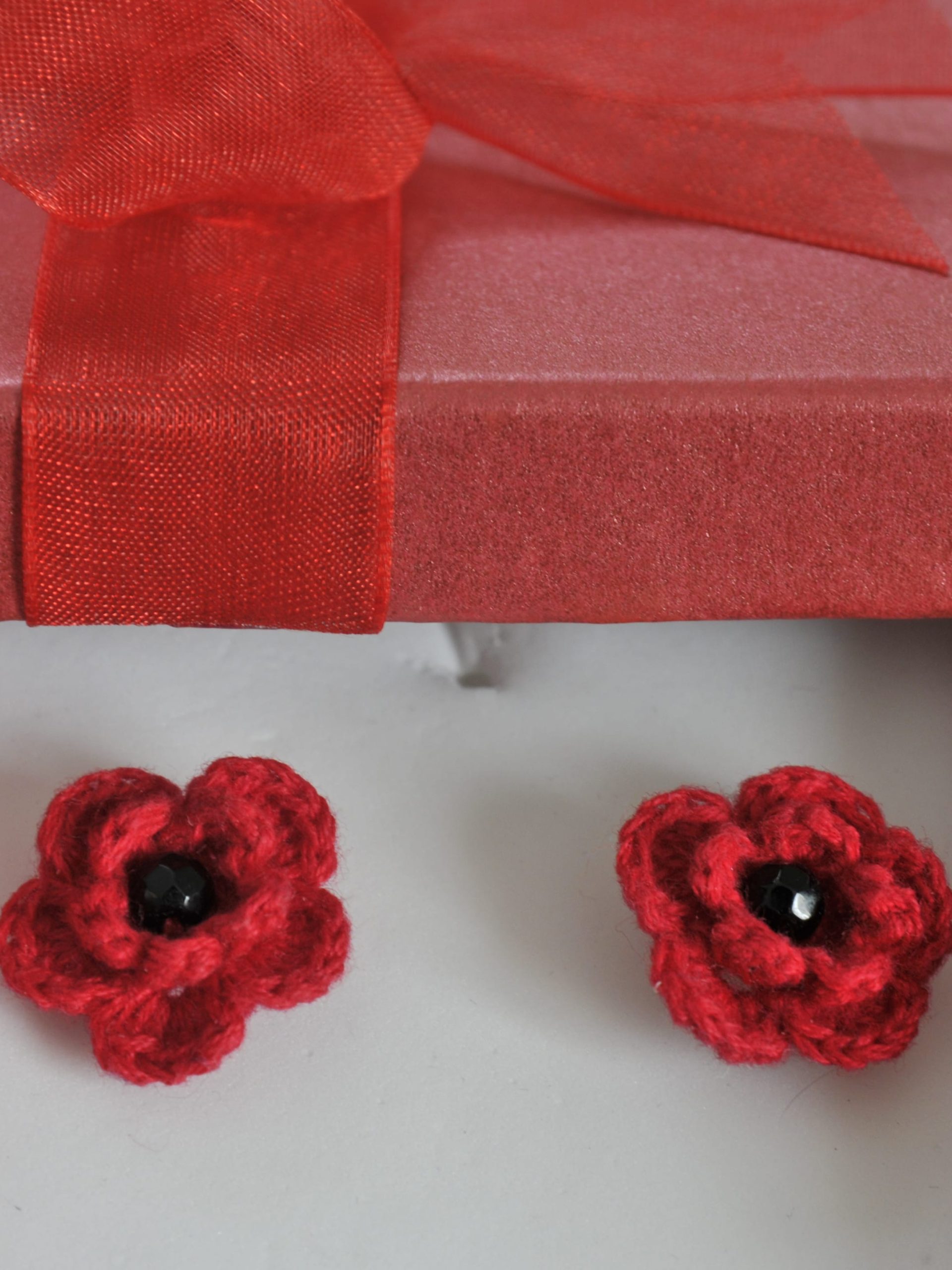 Handmade flower-shaped brooch with five petals of black beads set in silver wire and a center of red crystal beads, in a red gift box