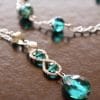 Emerald green teardrop crystal pendant with a matching silver chain bracelet and faceted beads on a dark brown background