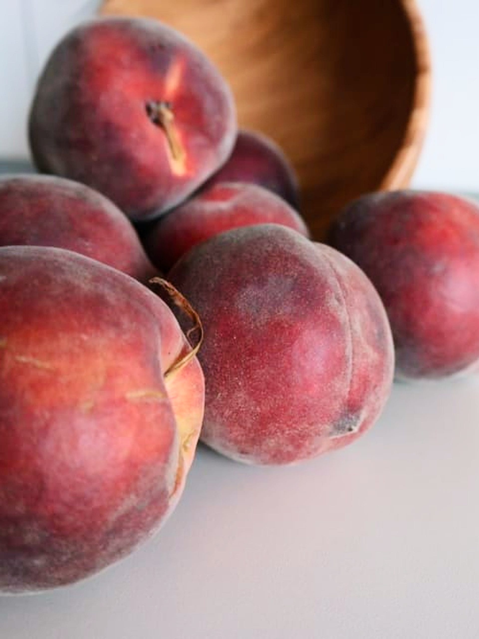 Fresh ripe red-blushed peaches next to a wooden bowl on a kitchen counter