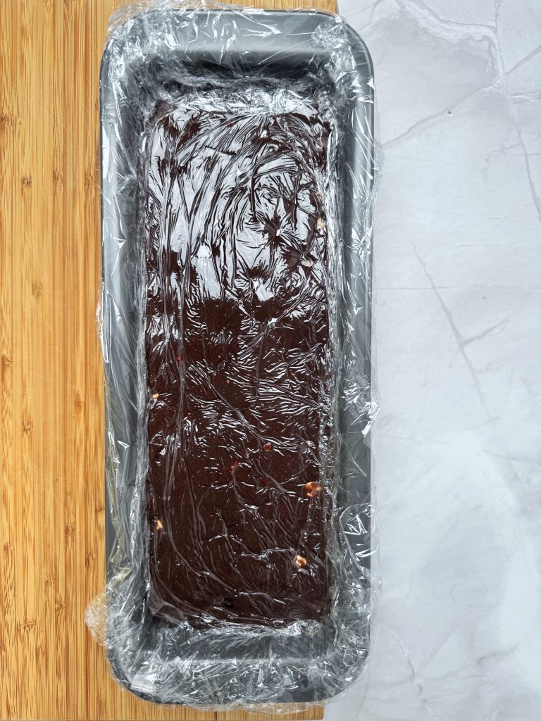 Homemade chocolate mixture in a loaf tin lined and covered with cling film
