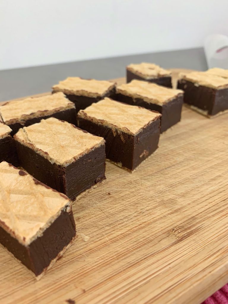 Squares of homemade chocolate between wafer sheets on a wooden cutting board