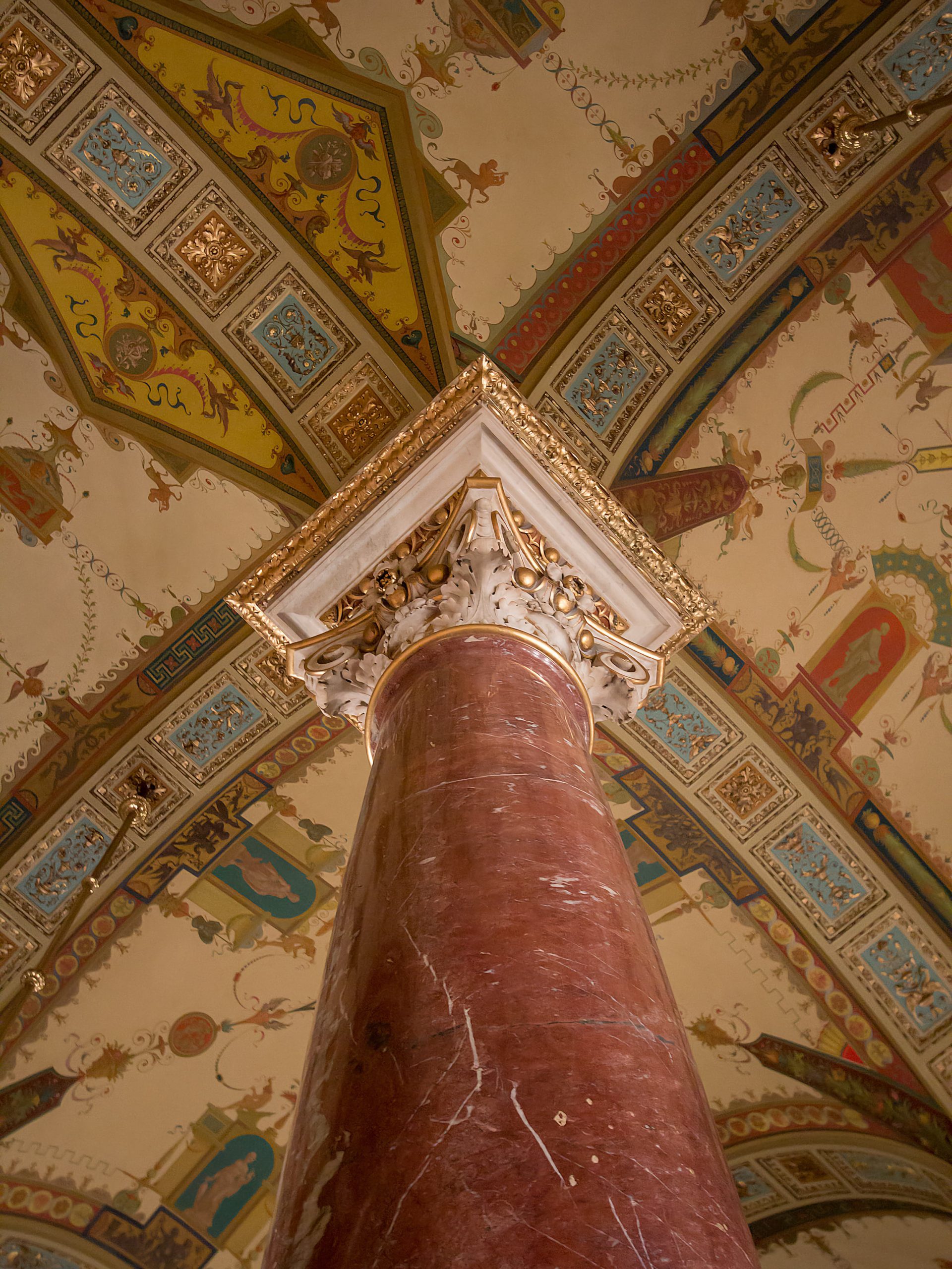 A reddish column rising to an ornate capital beneath a painted Opera House ceiling