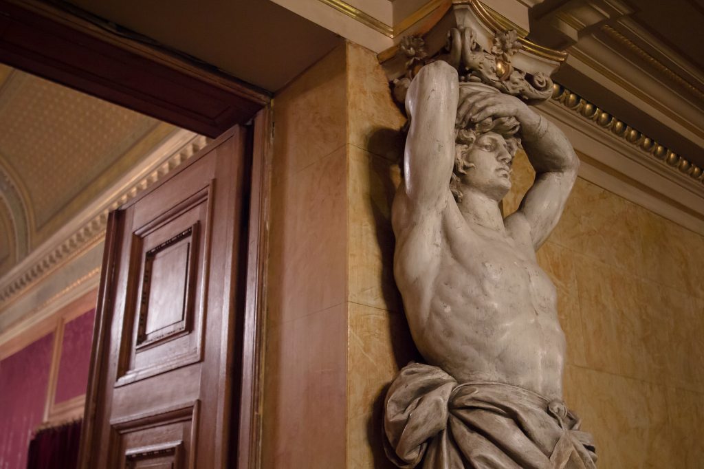 A sculpted male figure with raised arms beside a wooden doorway inside the Opera House