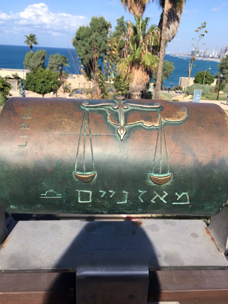 Placă metalică cu simbolul zodiei Balanță pe Podul Dorințelor din Jaffa, cu palmieri și marea &icirc;n fundal