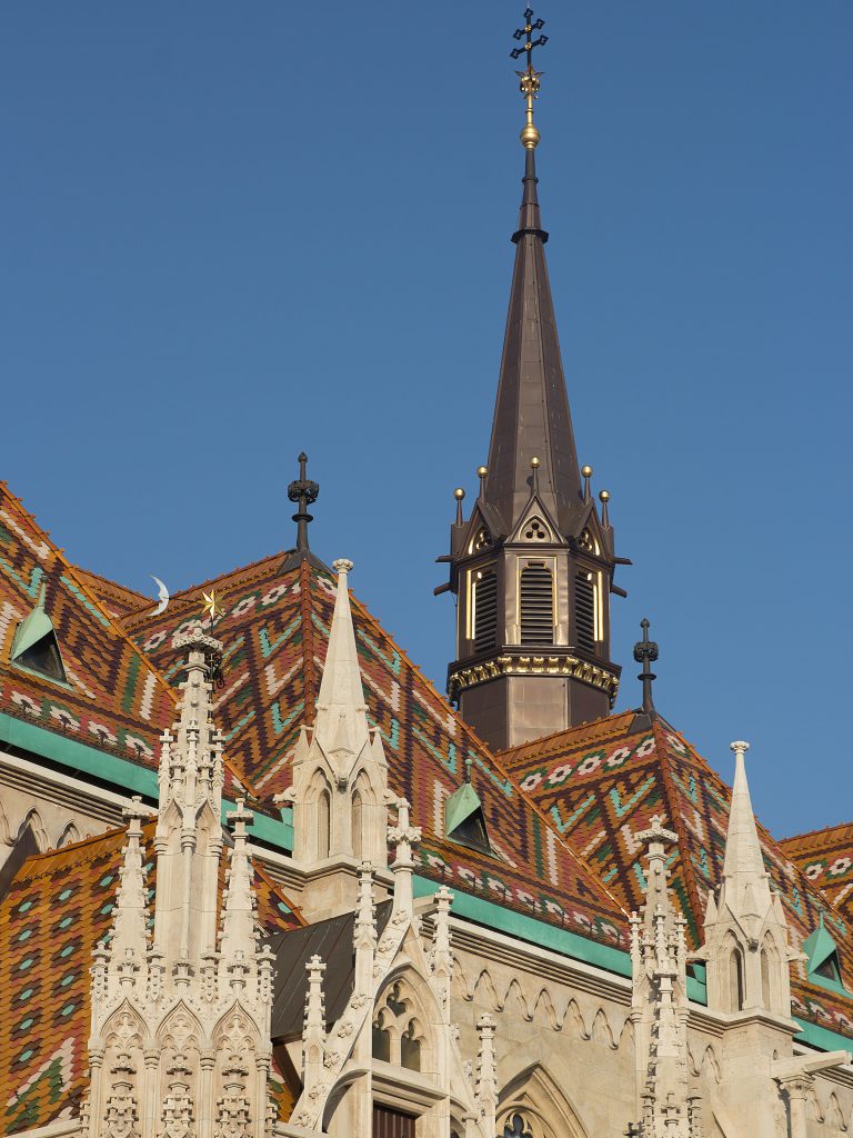 Geometric patterns on the colourful tiled roof of Matthias Church beside a slender spire