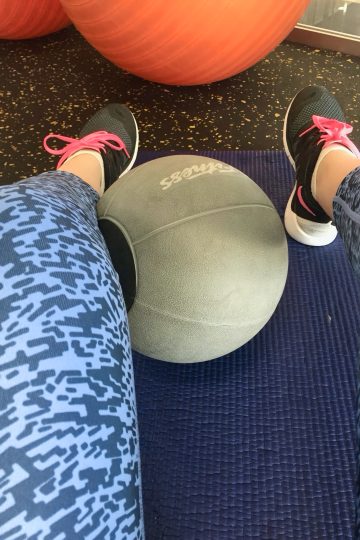 Minge medicinală pe o saltea mov, între picioare în colanți cu imprimeu și pantofi sport cu șireturi roz