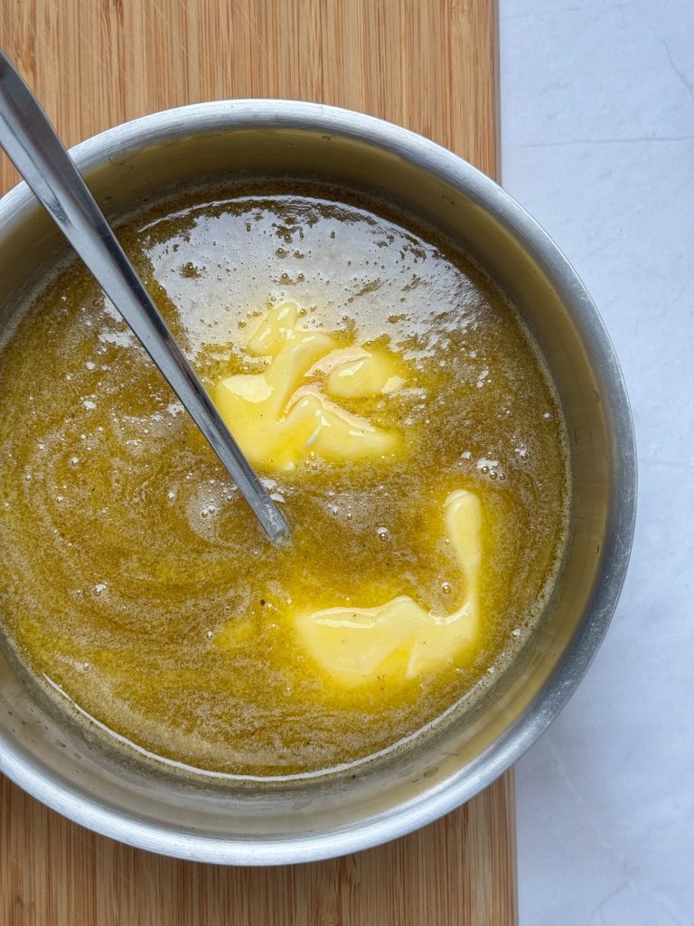 Pieces of butter melting into syrup in a saucepan with a metal spoon