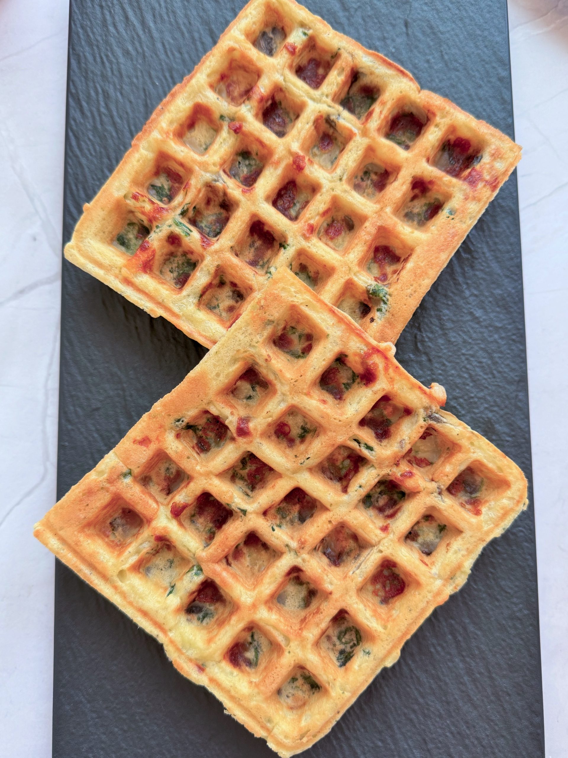 Două gofre sărate cu ciuperci, mozzarella și spanac, parțial suprapuse pe un platou negru, fotografiate de sus