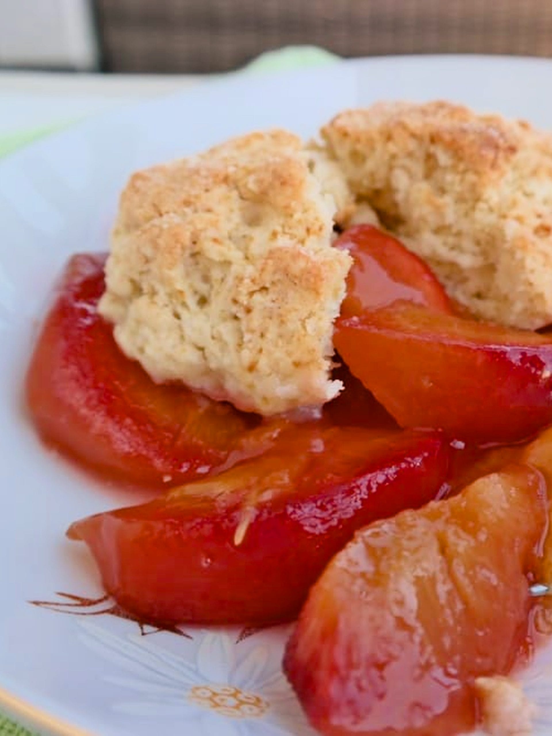 Serving of peach cobbler in a floral bowl with juicy peach slices and golden biscuit topping