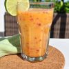 A glass of peach smoothie garnished with a lime slice, standing on a cork mat