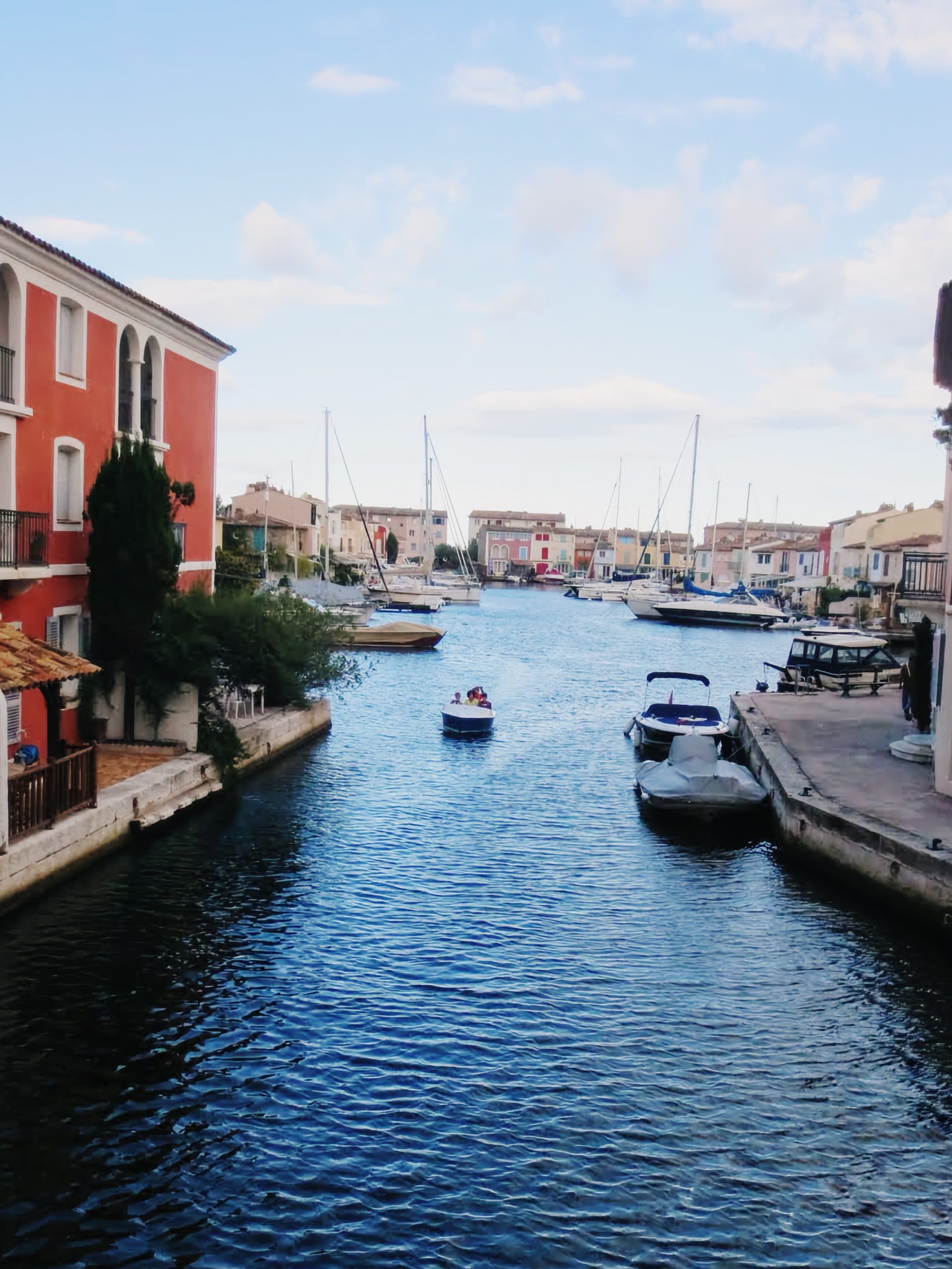 Bărci pe un canal din Port Grimaud, &icirc;ntre case colorate, sub un cer cu nori
