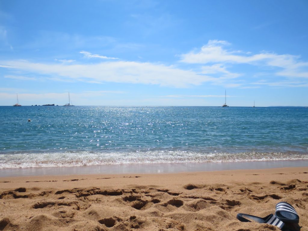 Plajă cu nisip &icirc;n Saint-Rapha&euml;l, cu marea albastră și c&acirc;teva ambarcațiuni &icirc;n depărtare