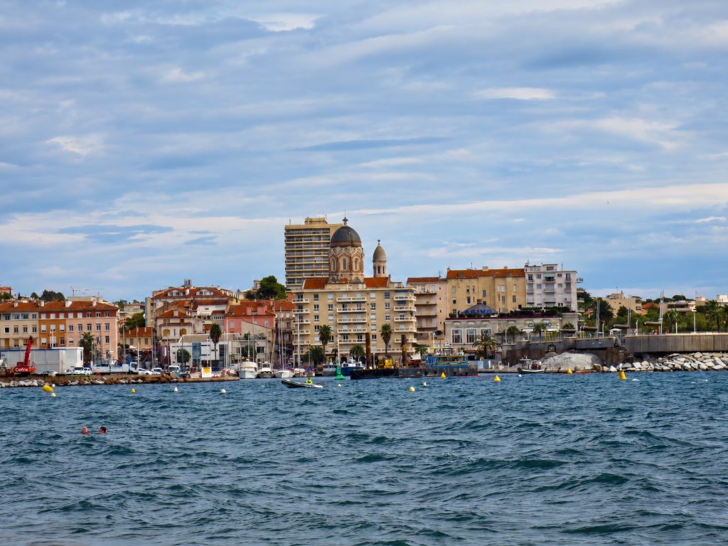 Clădiri pe malul mării &icirc;n Saint-Rapha&euml;l, cu o cupolă de biserică deasupra acoperișurilor și bărci &icirc;n port