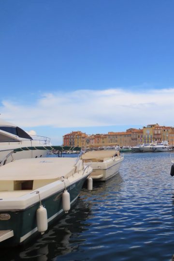 Bărci cu motor în portul din Saint-Tropez, cu fațade colorate și un turn de biserică în fundal