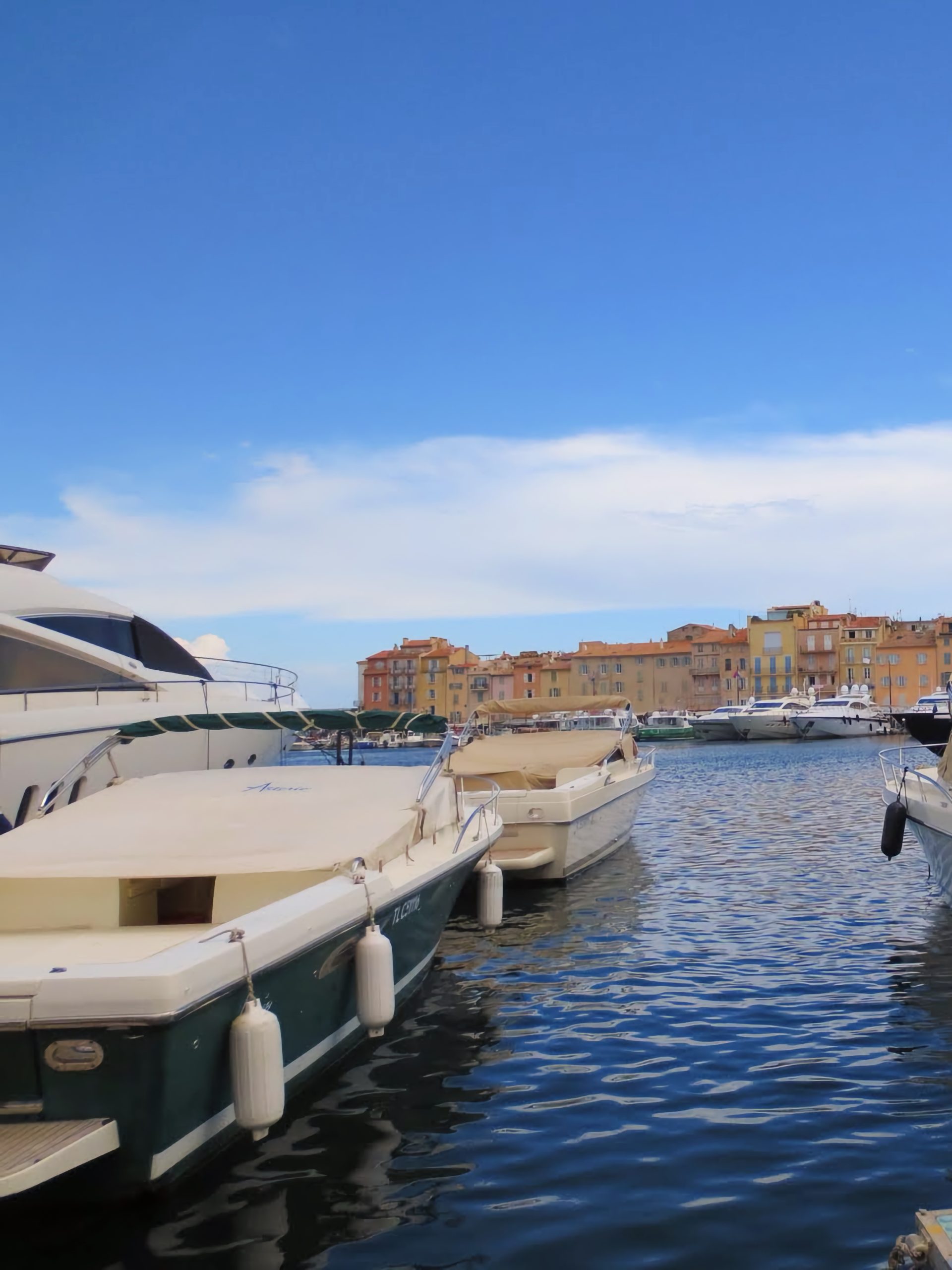 Bărci cu motor &icirc;n portul din Saint-Tropez, cu fațade colorate și un turn de biserică &icirc;n fundal