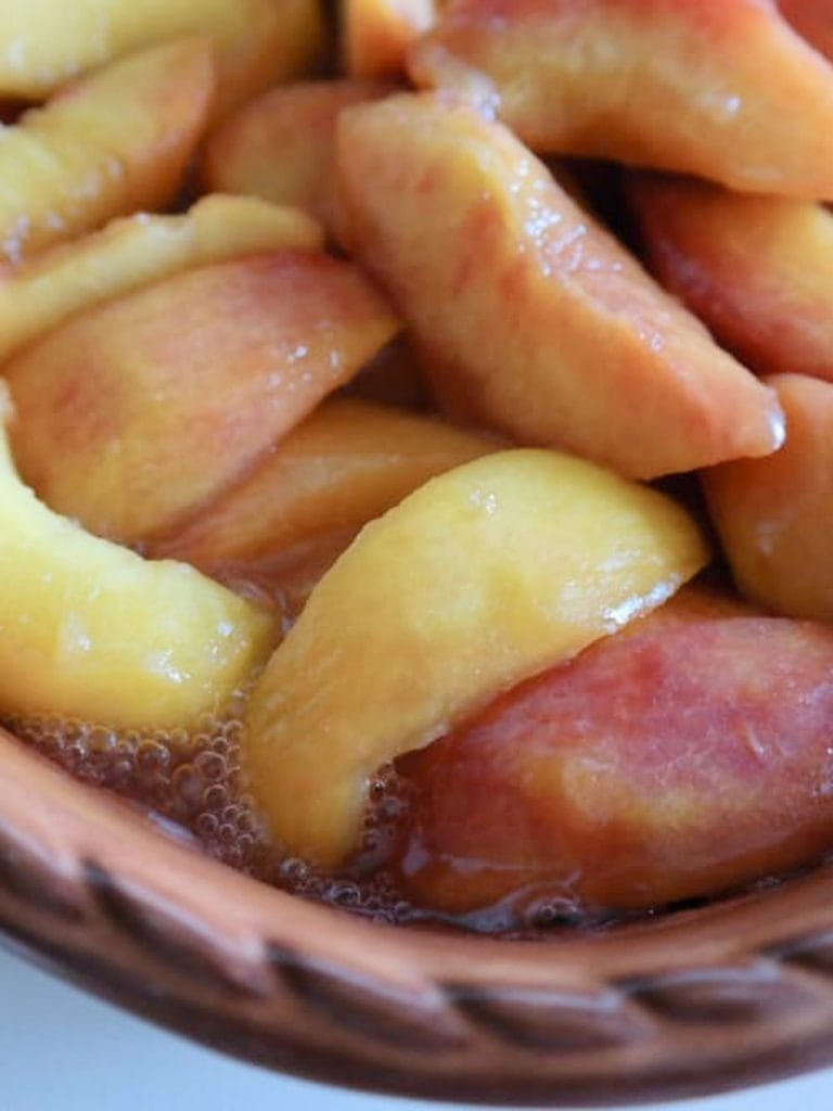 Sliced peaches with their juices in a terracotta baking dish, ready for cobbler