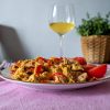 Pui picant cu ardei kapia și ouă, servit pe farfurie, alături de un pahar cu vin alb