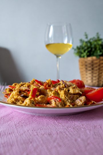 Pui picant cu ardei kapia și ouă, servit pe farfurie, alături de un pahar cu vin alb