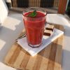 Pahar cu smoothie roșu și frunze de mentă, pe un tocător de lemn, lângă două bucăți de napolitană